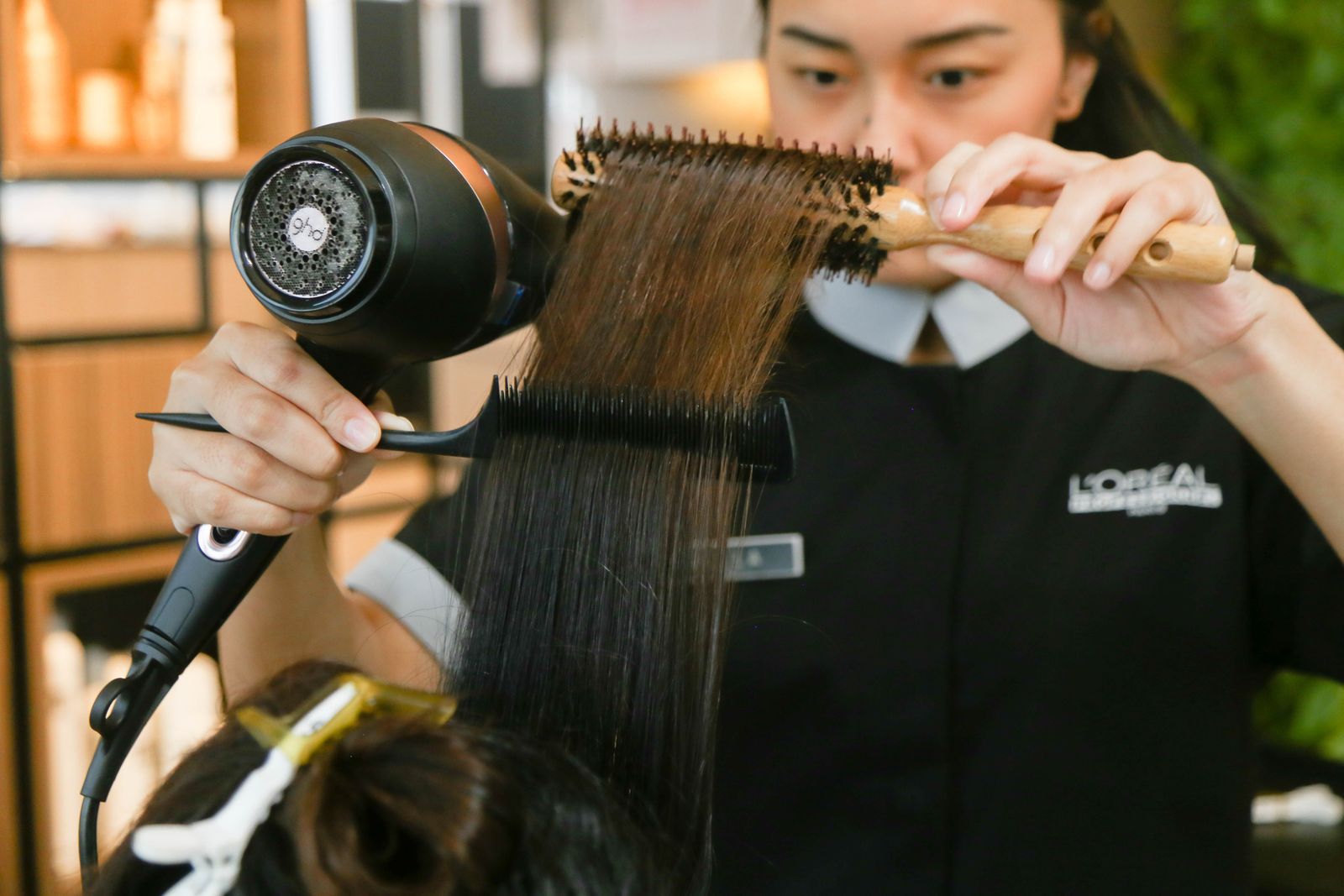 Stylistin föhnt und stylt Haare in hellem Tageslicht